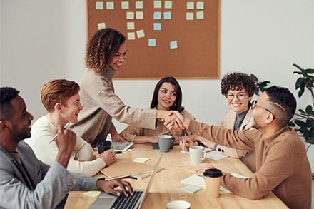 six people sitting at a table three men three woman one woman and man are shaking hands across the table