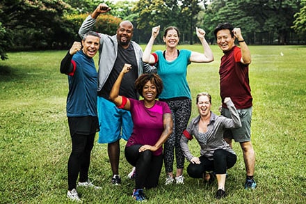 six people standing in a green field in activewear three women three men all flexing