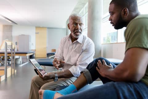 Impact wholesale: Doctor and Patient with ankle wrap sitting down talking with tablet with window in background angled view