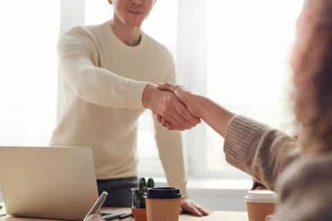 Ops: Man and woman shaking hands over desk with computer in front of a window