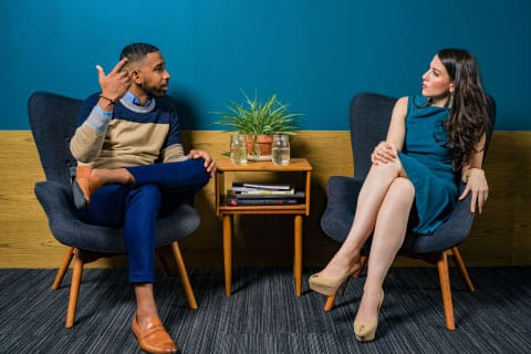 Sales: Man and woman talking in a pair of chairs with side table in the center